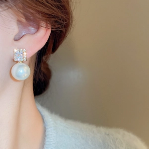 Close-up of elegant gold square diamond stud with large white pearl on woman's ear