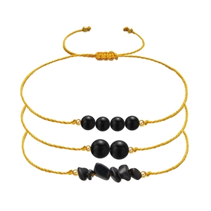 Detail of three-piece yellow braided rope bracelets with black stones and gold metal beads