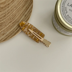 Macro detail of amber resin hair clip with gold glitter and metallic grip on white surface