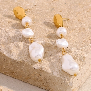 Detail of baroque pearl drop earrings with 18K gold irregular metal on a textured stone
