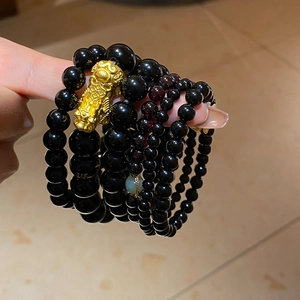Detail of obsidian beaded bracelet featuring a gold PiXiu charm and green jade accent