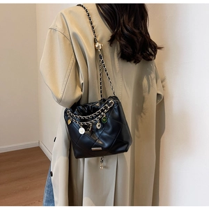 Quilted black bucket bag with gold chain strap shown on a model wearing a beige coat