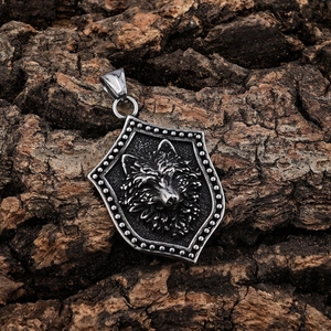 Detailed close-up of a silver Viking wolf shield pendant on a rustic wood bark surface