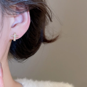 Close-up of a gold cross stud earring with sparkling cubic zirconia on a female model