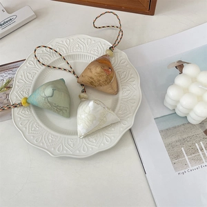 Three triangular zongzi fabric charms in green, brown, and white on a ceramic plate