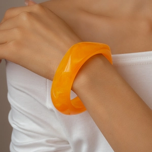 Close-up of bright orange resin bangle showing natural swirling textures on wrist
