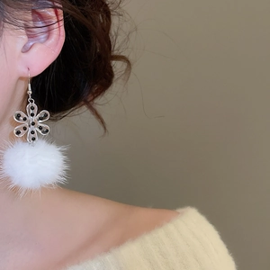 Detail of acrylic flower and white pom-pom drop earrings worn by a model