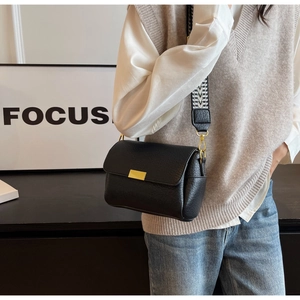 Détail du sac carré en cuir noir avec boucle dorée et bandoulière tissée large