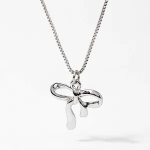 Detailed view of polished silver bow pendant with fine box chain jewelry texture