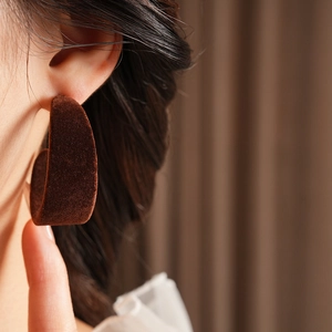 Close-up of minimalist C-shaped dark brown flocked earring worn by a model