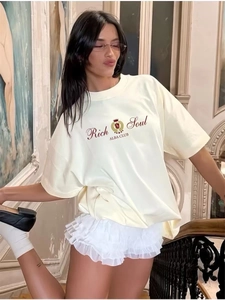 Λεπτομέρεια από κρεμ βαμβακερό t-shirt με κόκκινο λογότυπο και χαλαρή γραμμή