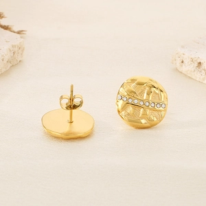 Detailed macro view of gold round earrings with pleated texture and sparkling crystal inlay