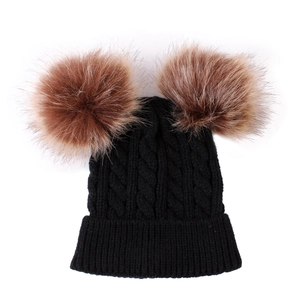 Close-up of black cable knit baby hat featuring double brown faux fur pom-poms