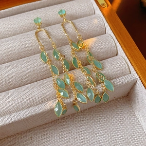 Détail de boucles d'oreilles à pompons et pendentifs feuilles vertes dans un coffret