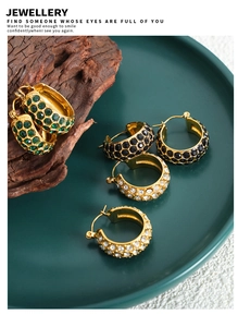 Close-up of C-shaped earrings with green, black, and white diamonds on a gold base