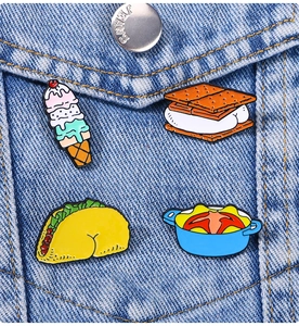 Detail of four creative enamel pins with humorous food designs on a blue denim jacket