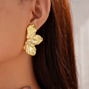 Close-up of a large gold irregular leaf-shaped acrylic earring worn by a female model