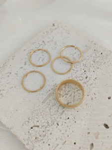 Set of minimalist golden stainless steel rings on a white textured stone surface