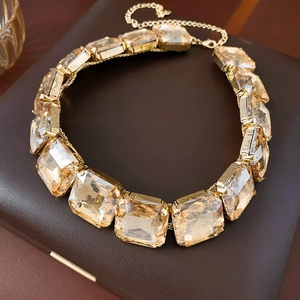 Dettaglio di una collana quadrata dorata con pietre champagne su pelle scura
