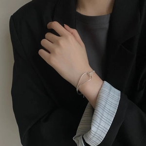 Detail view of a minimalist S925 sterling silver knotted heart bangle on a model wrist
