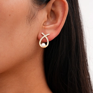 Close-up of elegant gold stud earrings with white pearl and sparkling crystals on model