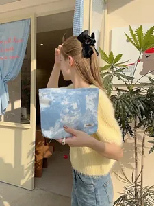Blue tie-dye fabric cosmetic bag with Sezakka label held by a hand in soft outdoor light