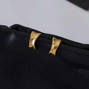 Macro view of wide concave 18K gold plated stainless steel earrings on black leather