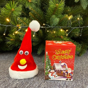 Cappello di Babbo Natale elettrico con scatola regalo davanti a un albero illuminato