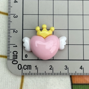 Macro view of a pink resin heart with yellow crown and white wings on a grid mat