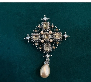 Detailed macro view of baroque cross brooch with champagne crystals and pearl drop charm
