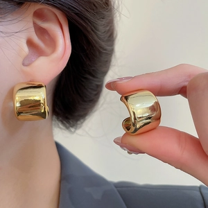 Detailed close-up of golden wide-surface round earrings with a polished mirror finish