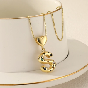 Macro view of gold S-letter pendant with colorful stones on white coffee cup
