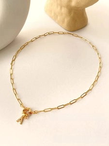 Detailed view of golden paperclip chain with zircon-paved letter A pendant on stone