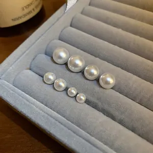 Minimalist white round pearl stud earrings in various sizes on a grey velvet jewelry tray