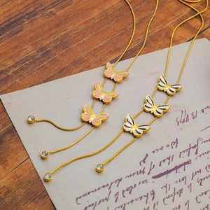 Detail of colorful enamel butterfly pendants on golden snake chain over vintage paper