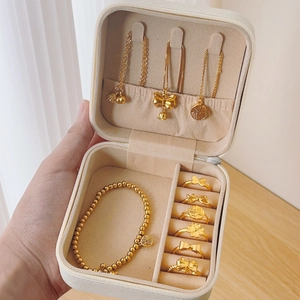 Portable cream jewelry storage box featuring ring slots, necklace hooks and golden charms