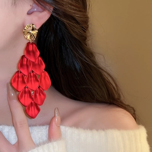 Close-up of model wearing exaggerated red acrylic petal tassel earrings with gold studs