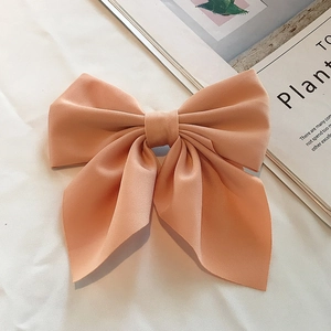 Flat lay macro view of a peach pink fabric bow hair clip on a soft white background
