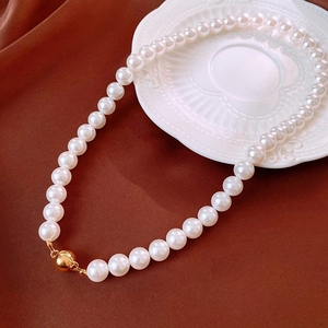 Detailed view of high-luster white pearl necklace with gold sphere clasp on silk
