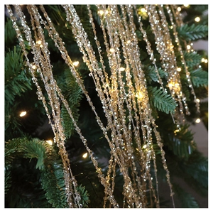 Macro shot of sparkling champagne gold beaded fringes draped on a green Christmas tree