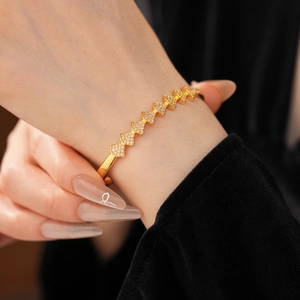 Detailed view of the gold-plated fan-shaped charm and zircon-studded clasp on a bangle