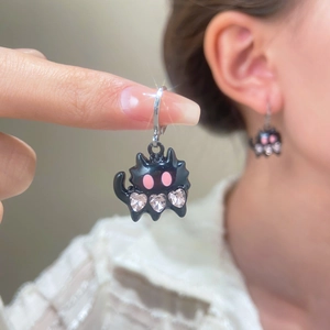 Detail showing black cat earrings with pink eyes and three sparkling heart-shaped crystals