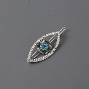 Exaggerated silver metal eye hair clip with blue and clear rhinestones on grey background
