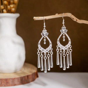 Close-up of ethnic silver peacock tassel earrings hanging on natural wooden branches