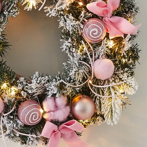Couronne de Noël illuminée avec nœuds roses, boules et lumières LED sur sapin enneigé