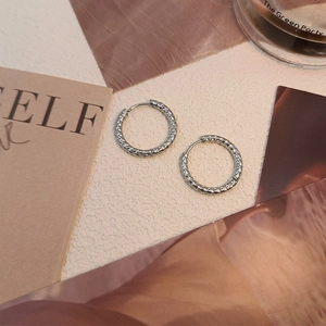 Detailed close-up of silver titanium steel hoop earrings with star-textured finish