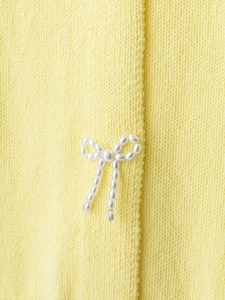 Detail of yellow knit cardigan featuring delicate bow decoration with lustrous white pearls