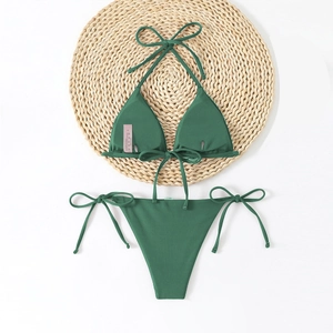 Flat lay of forest green ribbed bikini with triangle top and side-tie bottoms on straw mat
