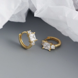 Macro view of gold huggie earrings featuring a square clear zircon on a soft white background