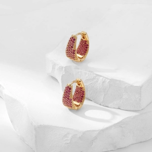Golden geometric hoop earrings with pink zircons displayed on a textured stone base